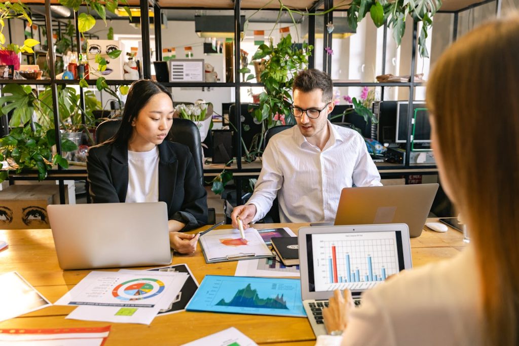 A diverse group of professionals collaborating in a business meeting with laptops and charts in a modern office setting.